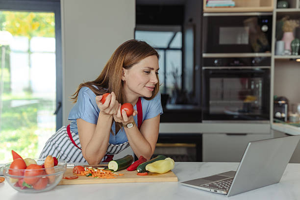 istock Beautiful woman cooking in a kitchen while watching a cooking tutorial on his laptop 2210294098