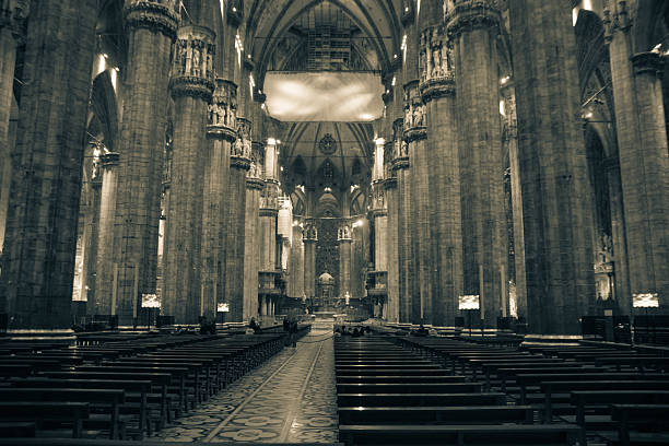 The interior of the Milan Cathedral (Duomo di Milano) with its towering columns and vaulted ceilings. The image captures the grandeur and intricate Gothic architecture.