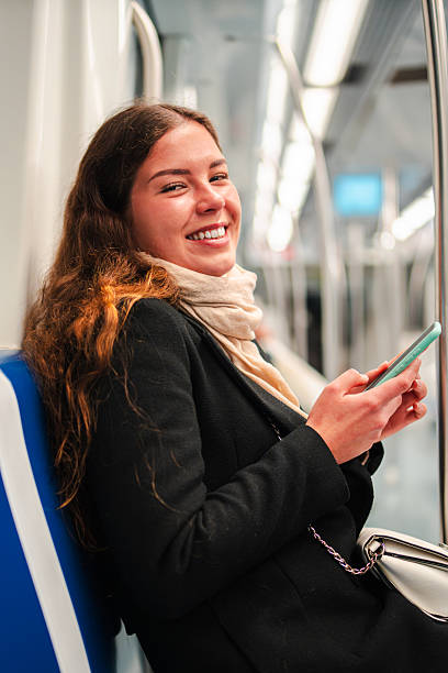 istock Joyful young woman engaged in browsing her smartphone while sitting comfortably on a subway train, enjoying her time as a passenger during her daily commute through the city streets 2210305074