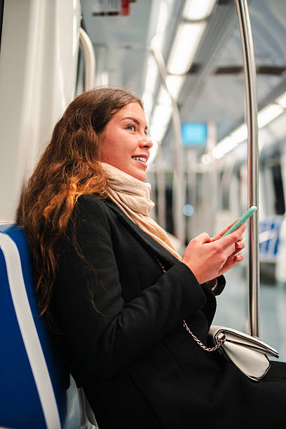 istock Young woman happily using her smartphone while sitting on the subway, enjoying her time as a passenger and browsing through various applications on her mobile device with a cheerful expression 2210306464