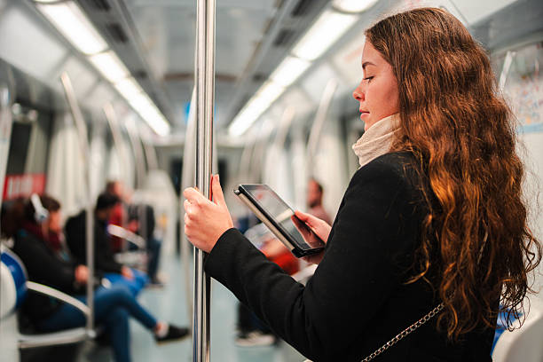 istock Focused woman reading an e-reader while standing in a subway train during her daily commute, immersed in the content of her device with a thoughtful expression on her face as she holds onto the pole 2210307883