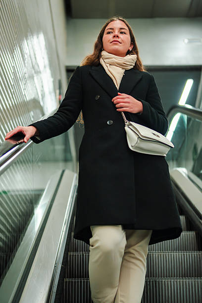istock Young woman confidently navigating the escalator while looking around in a bustling subway station with a stylish bag and a determined expression on her face as she moves towards her destination 2210307999