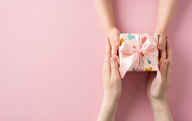 istock A beautifully wrapped pink gift box being exchanged between two people, symbolizing care and appreciation 2210311395