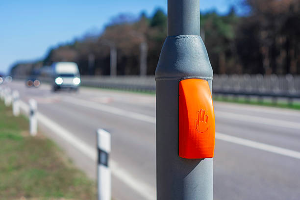 istock Orange pedestrian crossing button on a pole stands along a highway with a truck approaching in the background. Road safety and accessibility. 2210311417