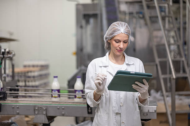 Female diary factory supervisor standing in front of conveyor belt and using digital tablet
