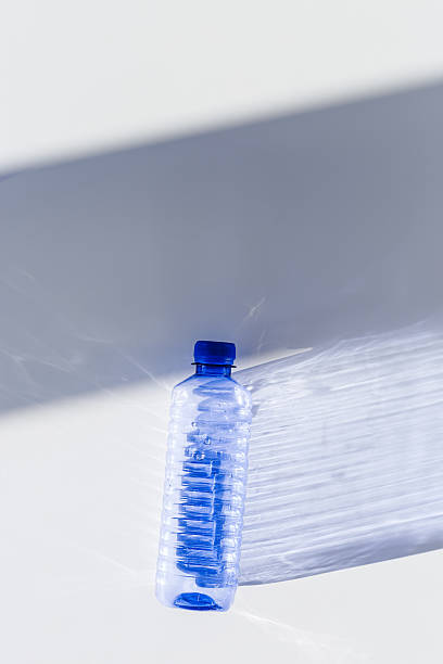 istock Transparent plastic bottles with blue caps and sun shadows on light background. Top view Water bottles at natural light. Themes of recycling, sustainability, water conservation, minimal style 2210328455