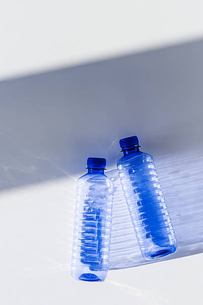 istock Blue plastic water bottles on white blue background with sunlight shadow and sun flare, Minimal top view photo, themes of ecology, recycling, sustainable living, reduce disposable plastics 2210328459