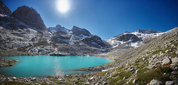 vibrant turquoise lake sits amid majestic mountains, reflecting bright sunlight. rugged terrain and clear skies create a stunning natural landscape, ideal for exploring and enjoying nature.