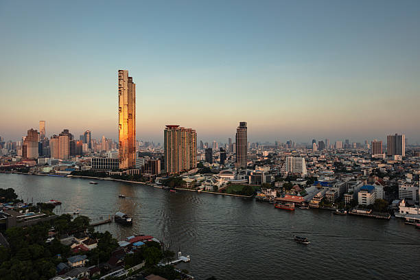 Elevated rooftop photograph of Bangkok's Chao Phraya River flowing in front of skyscrapers. Shot at sunset. This file is part of a series of shots taken at different times from the same location, matching shots are available.