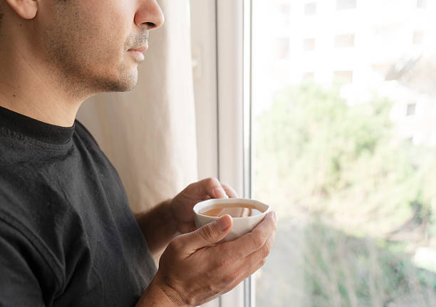 man having coffee and looking out of a window at home