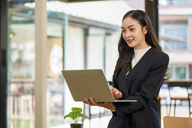 istock A young Asian businesswoman is standing at her desk using a laptop while working on a marketing strategy and business development plan in a modern office. 2210337776