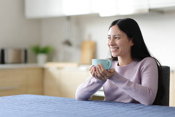 istock Asian woman drinking tea looking away at home 2210342521