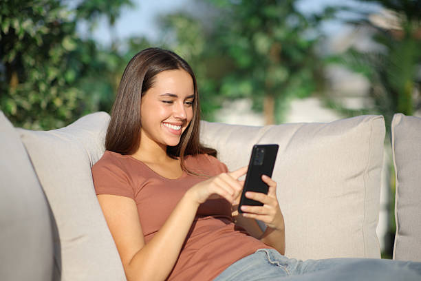 istock Happy woman using mobile phone sitting in sofa in a terrace 2210342620