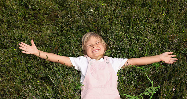 istock Smiling little girl lying on green grass outdoors, top view 2210343130