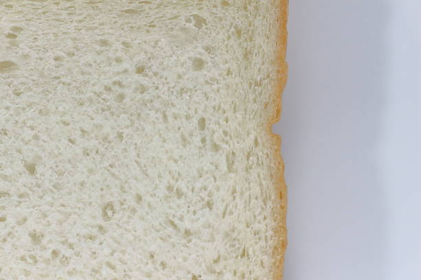 Stock photo featuring a sliced white bread loaf/loaves, symbolizing the essence of UPF ultra-processed food, set against a background of turquoise blue. The loaf of white is showed on its end, with the slices neatly arranged.