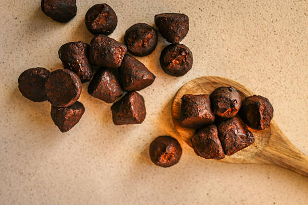 Stack of chocolate truffles on a wooden plate, one with a bite taken out, showing smooth filling and rich texture, with warm background lighting