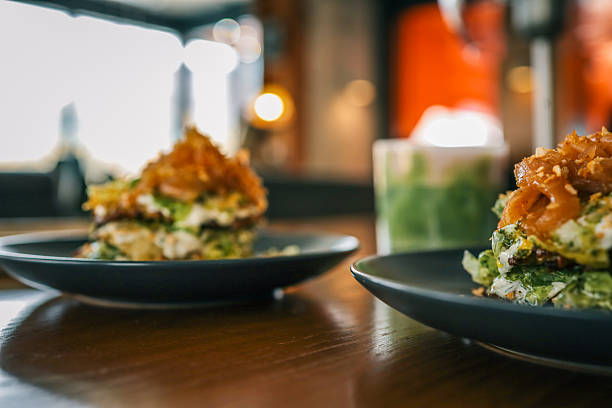 Close-up of a gourmet salad stack with creamy dressing and caramelized onions, served on a dark plate in a cozy modern cafÃ© setting with blurred background