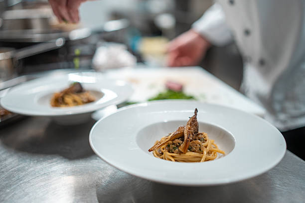 istock Elegant Plated Pasta Dish in Professional Kitchen with Chef Preparing Garnish Under Bright Lighting 2210347697