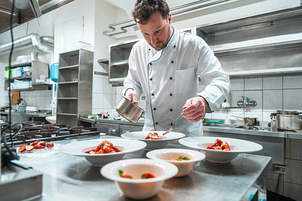 istock Male Chef in White Coat Plating Elegant Dishes in Modern Professional Kitchen 2210347713