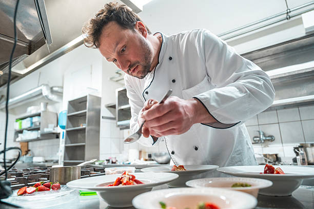 istock Focused Male Chef Plating Gourmet Dish in Professional Kitchen with Bright Lighting 2210347714