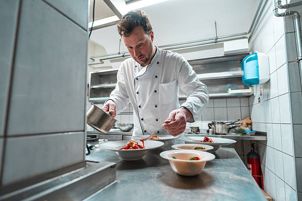 istock Focused Male Chef in White Uniform Plating Gourmet Dishes in a Professional Kitchen 2210347717