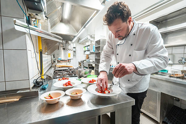 istock Male Chef Plating Gourmet Dish in Bright Professional Kitchen with Stainless Steel Elements 2210347722