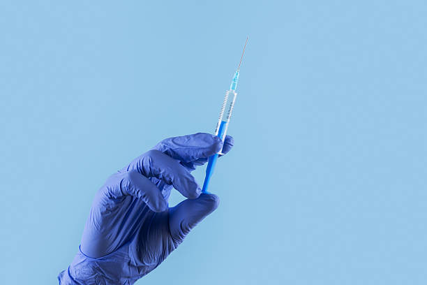 istock Doctors hand in surgical gloves holds a syringe on blue background 2210356584