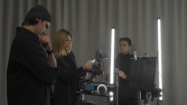 istock Female producer, camera operator and lighting technician in the studio during filming. The lighting technician adjusts the lighting, and the producer and cameraman discuss the shooting plan. 2210358195