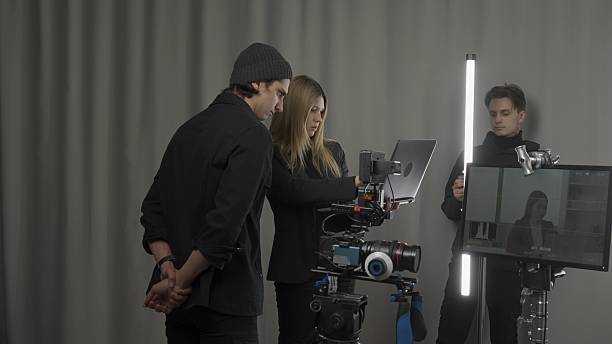 istock Female director, camera operator and lighting technician in the studio during filming. The lighting technician adjusts the lighting, the filmmaker and cameraman look at the shooting plan on the laptop 2210358292