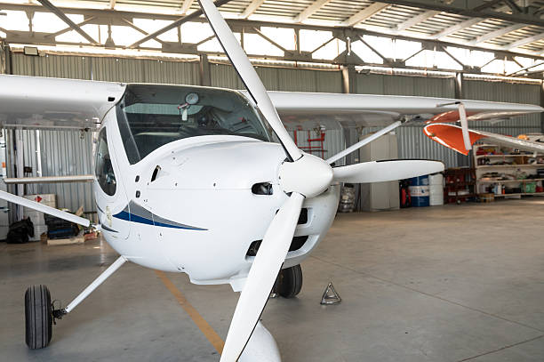 Close-up of a small white airplane with a propeller, parked in a hangar, showcasing its cockpit and wings.