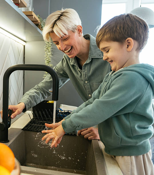 istock Lesbian mother with young adopted son washing hands in kitchen sink 2210359065