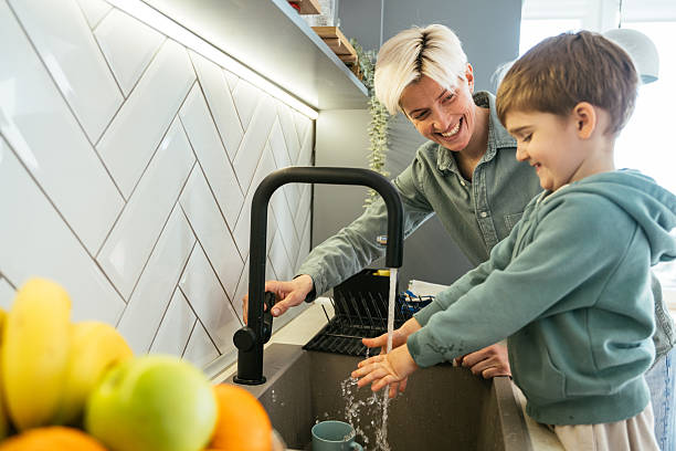 istock Lesbian mother with young adopted son washing hands in kitchen sink 2210359076