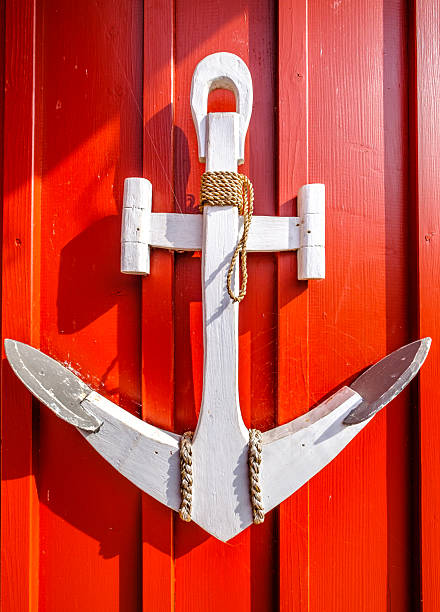 A prominent white anchor is affixed to a vivid red wooden wall, showcasing maritime decor in a coastal village during sunny daylight hours.
