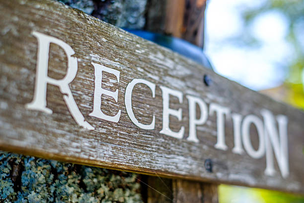 The wooden reception sign is prominently displayed at a charming location, set among lush greenery under bright daylight, welcoming guests.