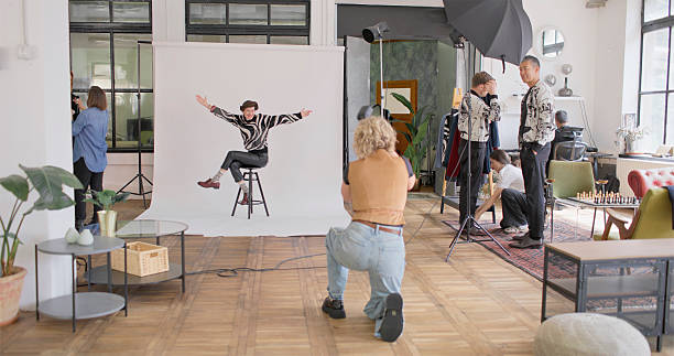 A bright indoor studio with diverse people, a photographer taking shots, and a lively background featuring props, natural light, and creative energy.