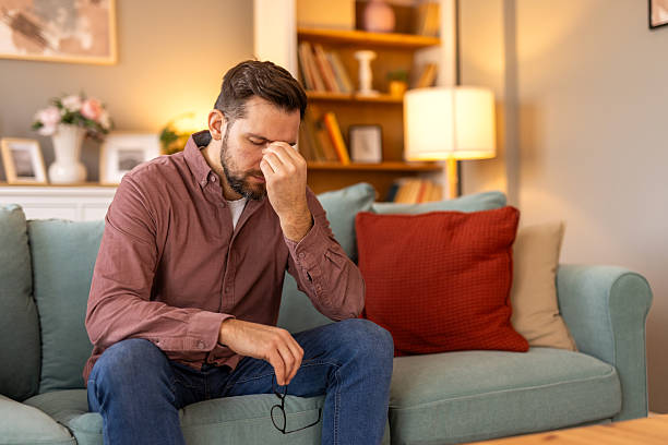 istock Closeup of man suffering from headache at home, touching his temples, copy space, blurred background. Migraine, headache, stress, tension problem, hangover concept 2210363839