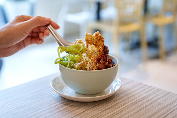 Malaysian cendol dessert with shaved ice, red beans, and palm sugar A traditional Malaysian cendol dessert served in a bowl with shaved ice, green jelly noodles, red beans, and palm sugar syrup. A hand scoops up the sweet treat indoors. red bean dessert stock pictures, royalty-free photos & images