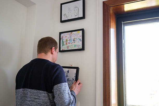 istock Father hanging daughter's drawings on the wall at home 2210364903