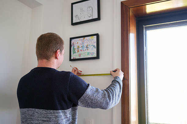 Father measuring wall to hang daughter's drawings