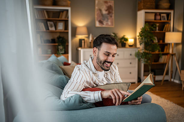 istock Young man relaxing on sofa reading a book at home 2210365234