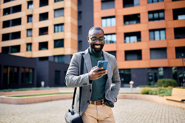 istock Smiling businessman using smartphone while walking near office building 2210367016