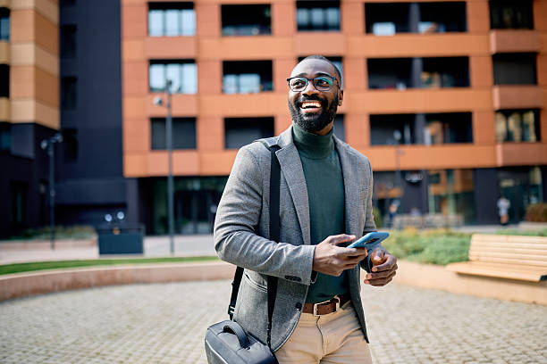 Smiling businessman walking and using smartphone in the city