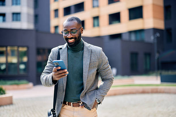 istock Smiling businessman using smartphone while walking near office buildings 2210367043