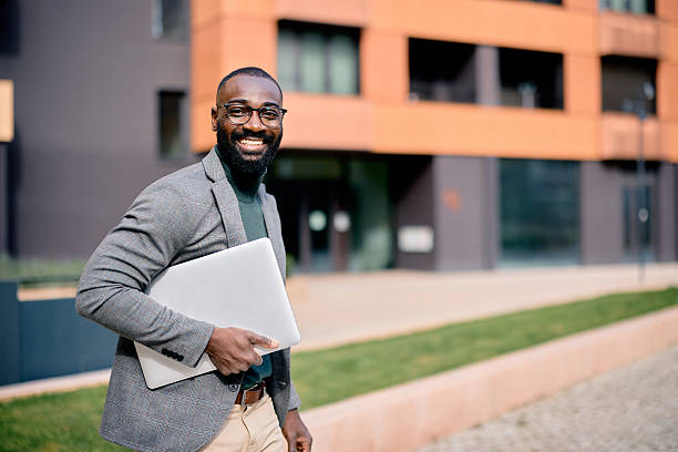 istock Smiling businessman walking outside office holding laptop 2210367067