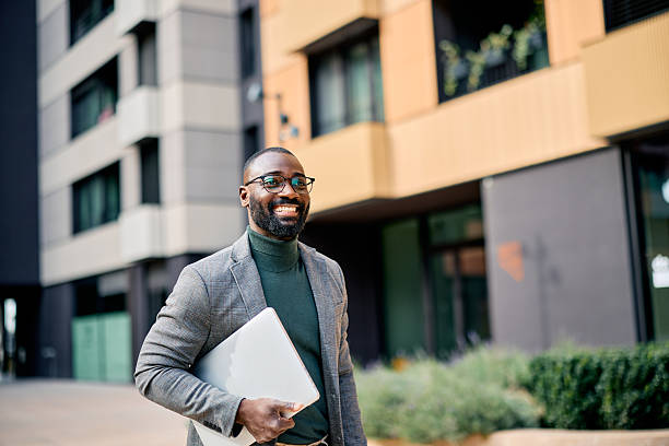 istock Smiling businessman walking outside holding a laptop 2210367080