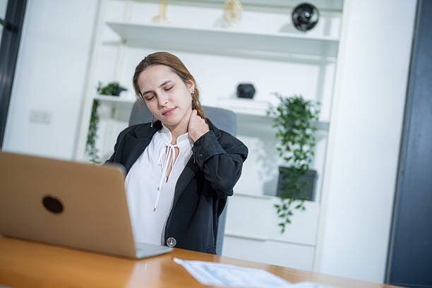 istock Woman experiencing neck pain while working at a desk in a modern office space during the afternoon 2210367283