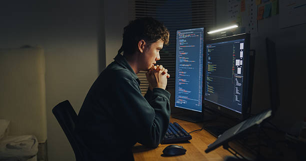 istock Young man software engineer experience emotional stress while working late on AI prompt coding on computer in bedroom at home night. Software developer, artificial intelligence and programmer. 2210368363