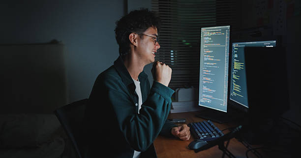 istock Young man software engineer expressing happiness after solving working late on AI prompts on computer in bedroom at home night. Software developer, artificial intelligence and programmer. 2210368425
