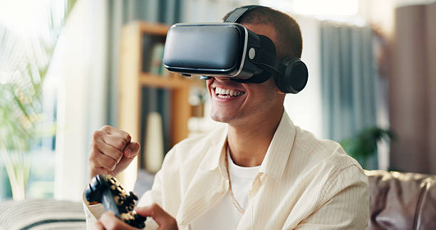istock Man, vr goggles and video game on sofa, happy and celebration in home for challenge in 3D metaverse. Person, augmented reality and glasses with futuristic ux, fist pump or cheers for winning in house 2210371114