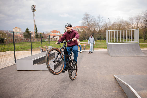 A mid adult Caucasian man performing a wheelie on his bicycle in a public outdoor skating park